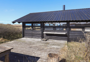 Buitenterras en zwart houten chalet bij vierpersoons vakantiehuis in Bindslev, Denemarken, in de natuur.