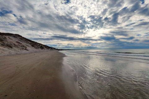 Strandansicht bei Bindslev, Dänemark mit sanften Wellen, breitem Sand und bewölktem Himmel.