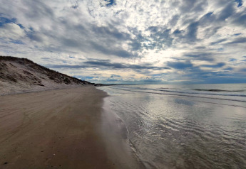 Strandansicht bei Bindslev, Dänemark mit sanften Wellen, breitem Sand und bewölktem Himmel.
