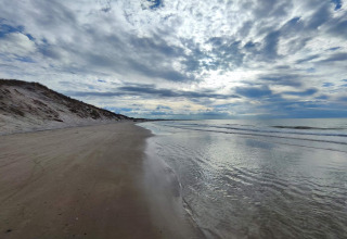 Billedet viser en rolig strand ved kysten nær Bindslev, Danmark, med dramatiske skyer og klitter.