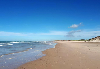 Foto eines ruhigen Sandstrands mit sanften Wellen und Dünen nahe einer Glamping-Unterkunft.