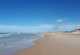 Billedet viser en fredelig strand ved en glamping-indkvartering med blåt hav, sand og klitter.