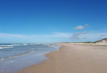 Foto eines ruhigen Sandstrands mit sanften Wellen und Dünen nahe einer Glamping-Unterkunft.