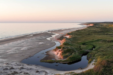 Blick auf einen Sandstrand mit einer geschwungenen Flussmündung und grüner Natur bei einer Glamping-Unterkunft.