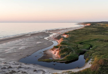 Panorama su spiaggia sabbiosa, ruscello tortuoso e vegetazione presso un alloggio glamping al tramonto.