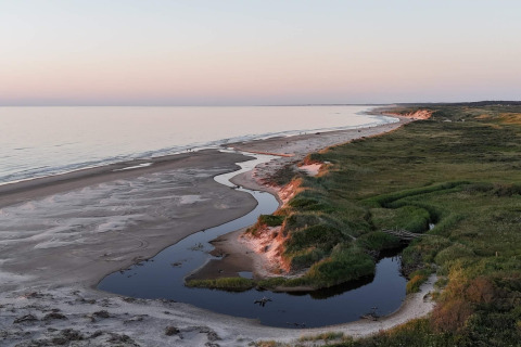 Udsigt over en sandstrand, snoet å og grøn vegetation ved glamping indkvartering ved kysten ved solnedgang.