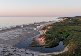 Blick auf einen Sandstrand mit einer geschwungenen Flussmündung und grüner Natur bei einer Glamping-Unterkunft.