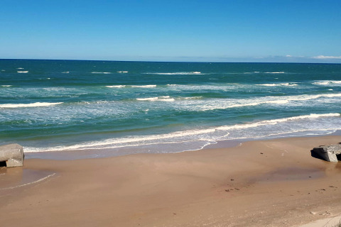 Blick auf das Meer, den Strand und Bunker bei einer Glamping-Unterkunft an einem sonnigen Tag.
