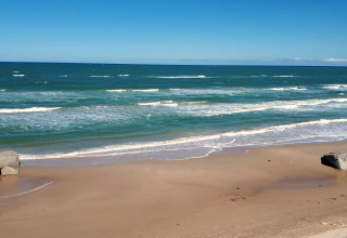 Udsigt til havet, strand og bunker ved glampingindkvartering på en solrig dag med blå himmel.