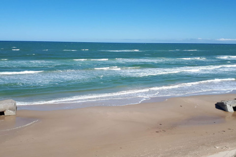 Blick auf das Meer, den Strand und Bunker bei einer Glamping-Unterkunft an einem sonnigen Tag.