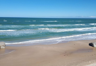 Blick auf das Meer, den Strand und Bunker bei einer Glamping-Unterkunft an einem sonnigen Tag.