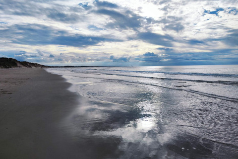 Ruhiger Strand mit sanften Wellen und bewölktem Himmel, aufgenommen bei einer Glamping-Unterkunft am Meer.