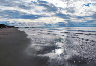 Ruhiger Strand mit sanften Wellen und bewölktem Himmel, aufgenommen bei einer Glamping-Unterkunft am Meer.