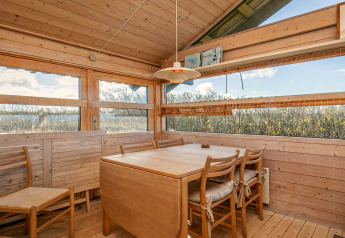 Essbereich in einem Chalet in Bindslev, Dänemark, mit Holzdekor und Panoramafenstern zur Natur.