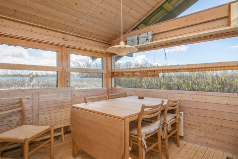 Lyst spiseområde i chalet i Bindslev, Danmark, med træinteriør og store vinduer med udsigt.