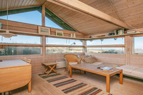 Helles Wohnzimmer im Chalet mit Holzmöbeln und Panoramafenstern, Blick auf Dünenlandschaft in Bindslev, Dänemark.