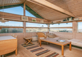 Helles Wohnzimmer im Chalet mit Holzmöbeln und Panoramafenstern, Blick auf Dünenlandschaft in Bindslev, Dänemark.