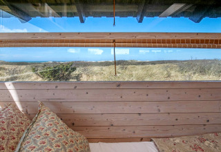 Blick aus dem Bett im Ferienhaus in Bindslev, Dänemark, mit Fenster zur Dünenlandschaft und Himmel.