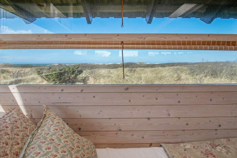Blick aus dem Bett im Ferienhaus in Bindslev, Dänemark, mit Fenster zur Dünenlandschaft und Himmel.