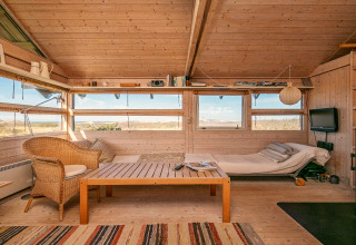 Indbydende stue i et sommerhus i Bindslev, Danmark, med lyst træinteriør, sofa og udsigt til naturen.