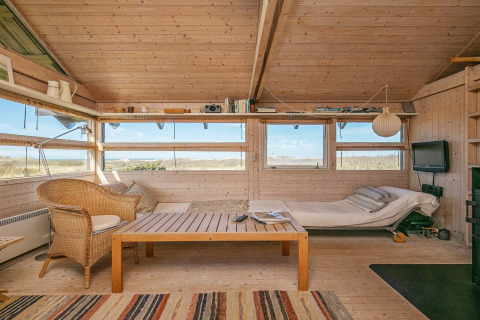 Indbydende stue i et sommerhus i Bindslev, Danmark, med lyst træinteriør, sofa og udsigt til naturen.