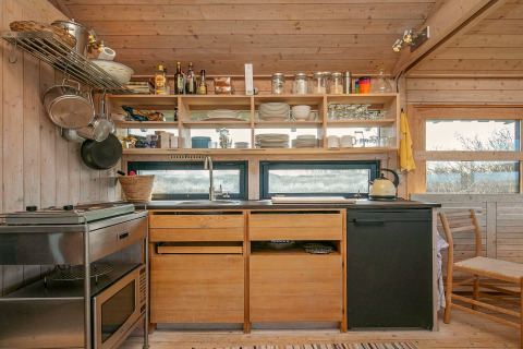 Gemütliche Holzküche in einem Ferienhaus in Bindslev, Dänemark, mit offenen Regalen und Blick nach draußen.