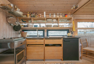 Hyggeligt træ-køkken i et sommerhus i Bindslev, Danmark, med åbne hylder, potter og naturskøn udsigt.