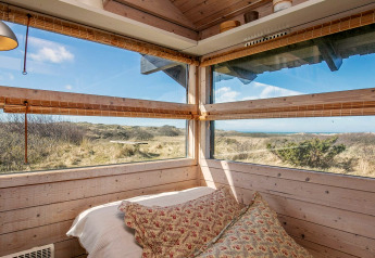 Bedroom with large windows and scenic nature view in a holiday chalet in Bindslev, Denmark, on a sunny day.