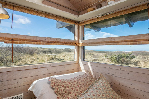Schlafzimmer mit Panoramafenstern und Naturblick in einem Ferienhaus in Bindslev, Dänemark bei Sonne.
