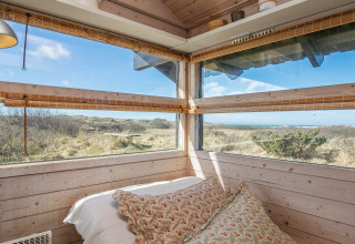 Schlafzimmer mit Panoramafenstern und Naturblick in einem Ferienhaus in Bindslev, Dänemark bei Sonne.