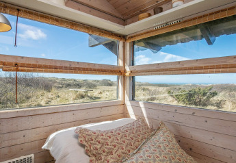 Chambre avec grandes fenêtres et vue sur la nature dans un chalet à Bindslev, Danemark, par une journée ensoleillée.