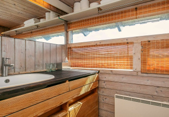Wood-paneled bathroom with sink, wooden cabinets, mirror, and bamboo blinds in chalet in Bindslev, Denmark.