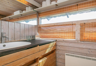 Træbeklædt badeværelse med håndvask, træskabe, spejl og rullegardiner i chalet i Bindslev, Danmark.