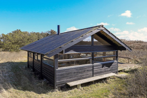 Schwarzes Holzchalet für 4 Personen in Bindslev, Dänemark, inmitten von Natur und unter blauem Himmel.