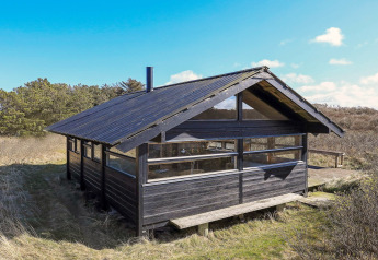 Black wooden 4 person holiday home in Bindslev, Denmark, surrounded by nature under a blue sky.