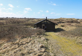Firepersoners feriehus i Bindslev omgivet af klitlandskab under en blå himmel med enkelte skyer.