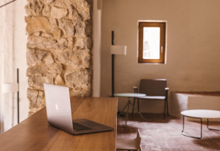 Espacio de trabajo moderno con escritorio de madera, portátil y pared rústica en Cala Montgó, Cataluña