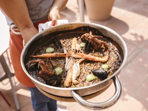 Une personne tient une poêle de fruits de mer à Wecamp Cala Montgó, parc de vacances en Catalogne, Espagne.