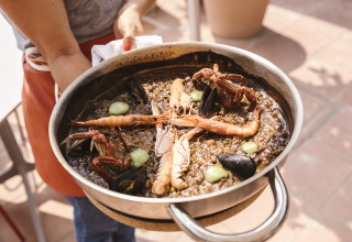 Una persona sostiene una sartén de mariscos en Wecamp Cala Montgó, un parque vacacional en Cataluña, España.