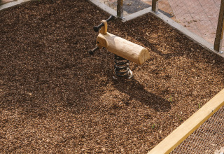 Eingezäunter Spielplatz mit Holzfederwippe auf Mulchboden, Vogelperspektive in Wecamp Cala Montgó.