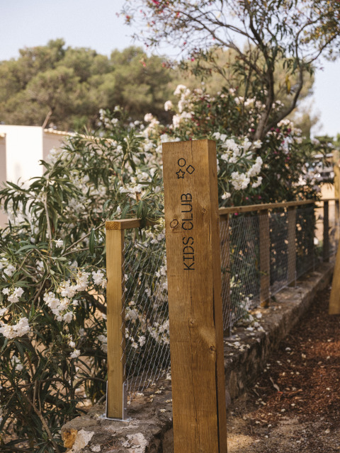 Houten bord met opschrift 'Kids Club' in vakantiepark Wecamp Cala Montgó, Catalonië, Spanje, tussen bloemen.