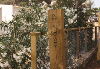 Houten bord met opschrift 'Kids Club' in vakantiepark Wecamp Cala Montgó, Catalonië, Spanje, tussen bloemen.