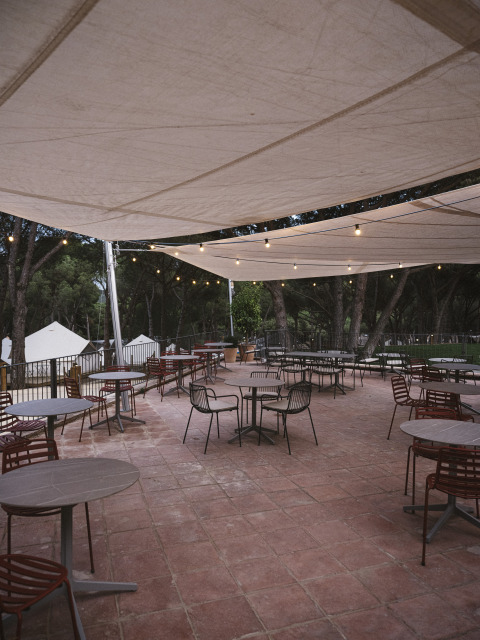 Terrasse im Wecamp Cala Montgó, Katalonien, Spanien, mit Tischen, Stühlen und Lichterketten am Abend.
