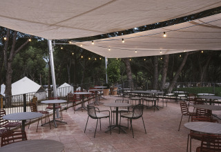 Udendørs terrasse på Wecamp Cala Montgó i Catalonien, Spanien, med tomme borde og stole under markiser.