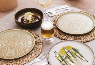 Mesa al aire libre en Wecamp Cala Montgó con plato de sardinas, vino, cerveza y platos vacíos al sol.