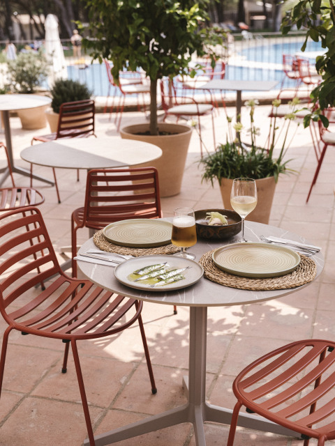 Table de café en plein air avec nourriture et boissons près de la piscine, entourée de chaises rouges à Wecamp Cala Montgó.