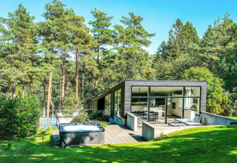 Moderne feriebolig til 8 personer i Ebeltoft med store vinduer, omgivet af grøn natur og træer.