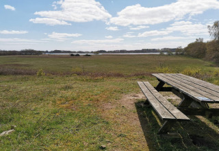 Foto van een houten bank en tafel bij een lodge, met uitzicht op een veld en bomen onder blauwe lucht.