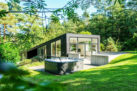 Modernes Ferienhaus in Ebeltoft, Dänemark, mit Whirlpool und Glasfront inmitten bewaldeter Natur.