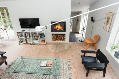 Modernes Wohnzimmer in einem Ferienhaus in Ebeltoft mit Kamin, Glastisch, Bücherregal und Designerstühlen.